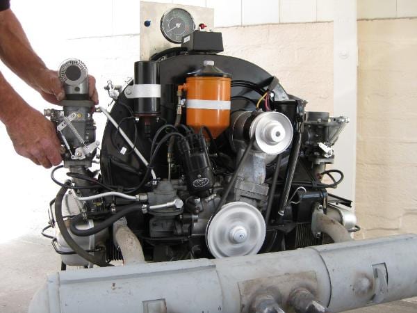 A Porsche 356 engine fitted with Zenith 32 NDIX carburetors mounted on a test stand, with a person adjusting one carburetor.